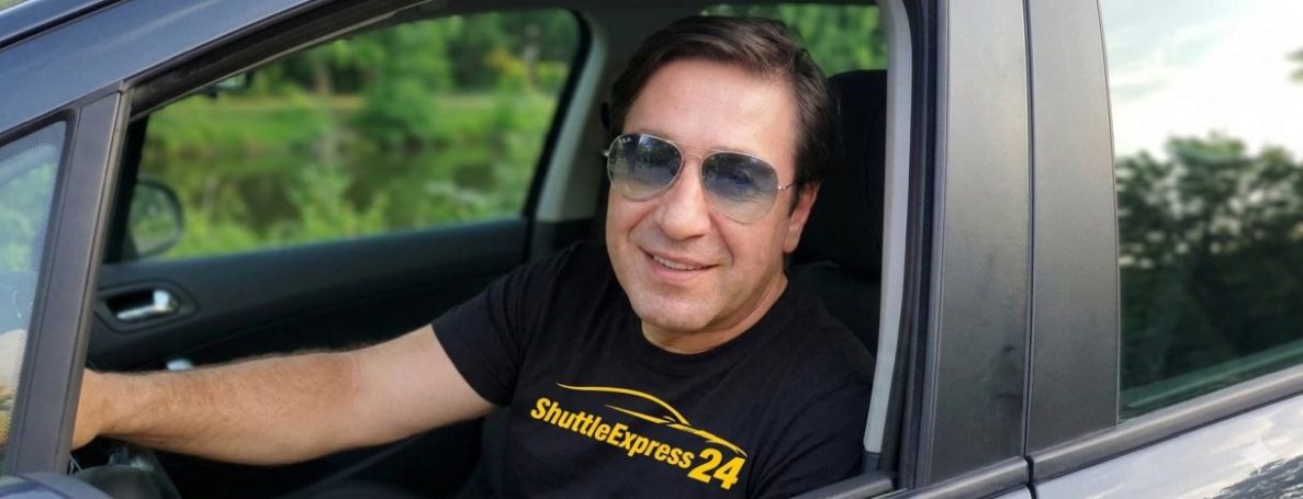 Mann mit Sonnenbrille sitzt im Auto und lächelt.