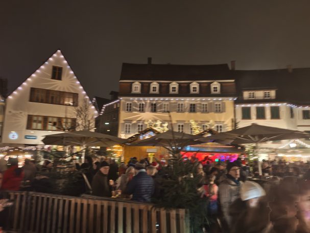 Beleuchteter Weihnachtsmarkt mit Menschen und festlich geschmückten Ständen.