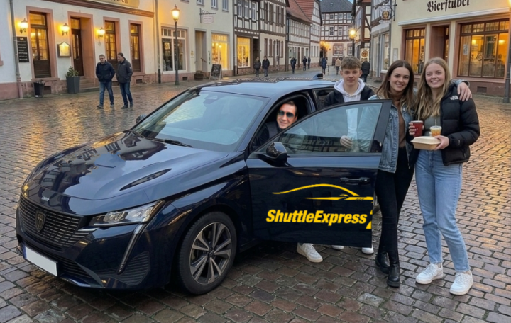 Drei Personen stehen neben einem schwarzen Auto in einer historischen Stadt.